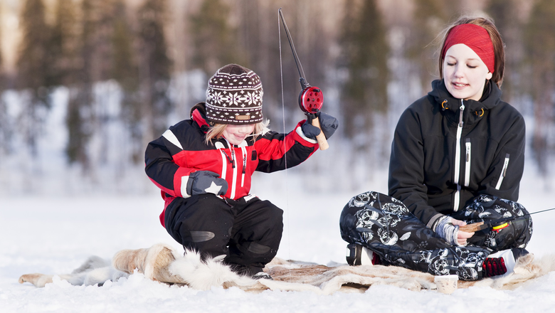 ett barn och en ungdom sitter på ett renskinn på isen och pimplar