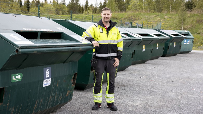 En glad man i varselkläder framför containrar för avfall