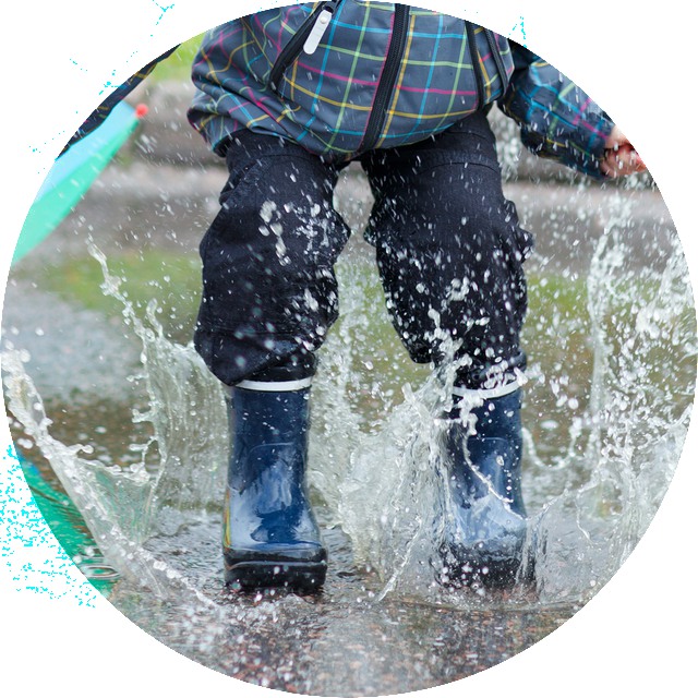Playful boy jumping in puddle on rainy autumn day