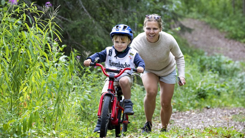 kvinna hjälper pojke på cykel uppför backe. det är sommar.