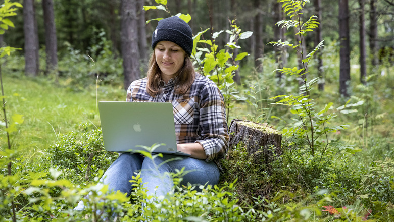 En kvinna mitt i skogen med en dator i knät.