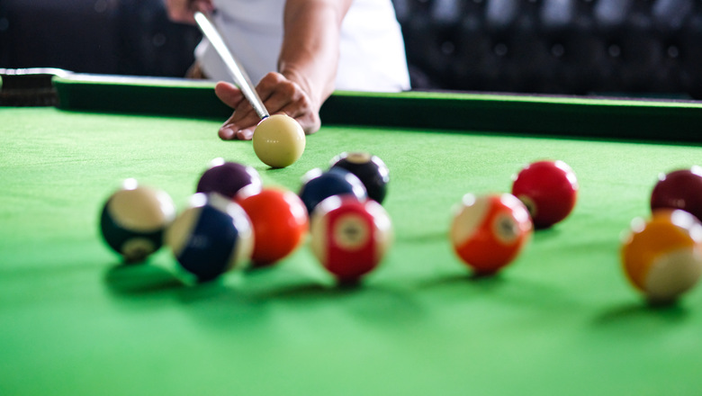 Mans hand and Cue arm playing snooker game or preparing aiming to shoot pool balls on a green billiard table. Colorful snooker balls on green frieze