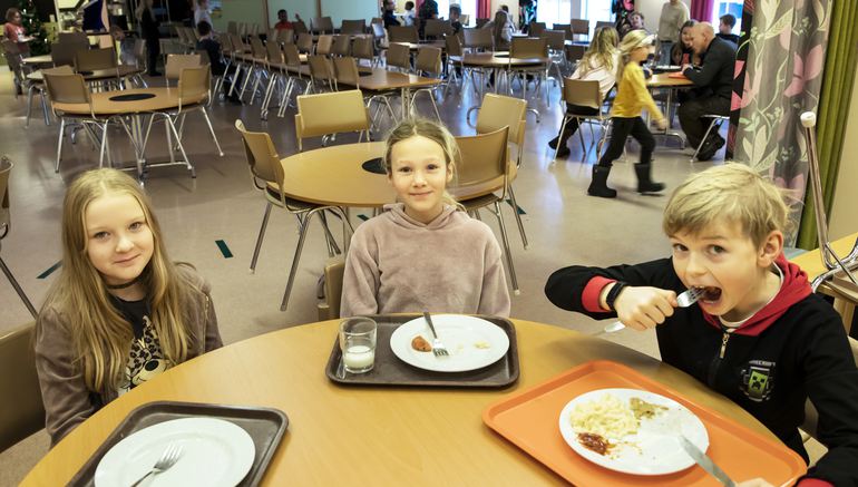 Tre barn i skolmatsal som äter 