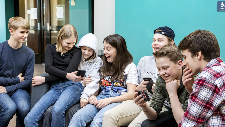 Sju glada ungdomar från klass 8 på Nyhedens skola sitter tillsammans i en soffa och kollar på sina mobiler