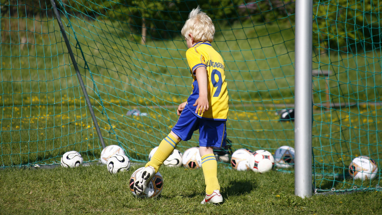 Lite pojke i svensk landslagsdräkt spelar fotboll.