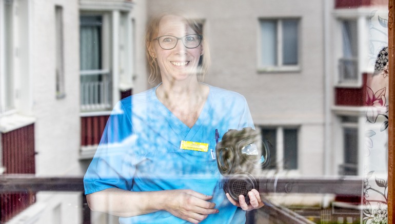 Kvinna bakom ett fönster med en skyddsmask i handen