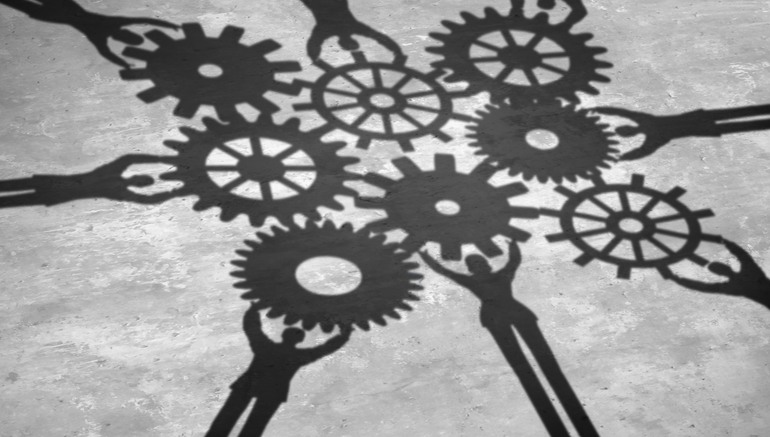 People teamwork holding gears connected together as a social community group symbol or business concept working for a common cause with cast shadows holding a cogwheel network in a corporate team partnership.