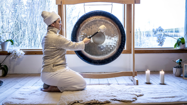 En kvinna på knä på en yogamatta och slår i en gong-gong. Tända ljus på golvet.