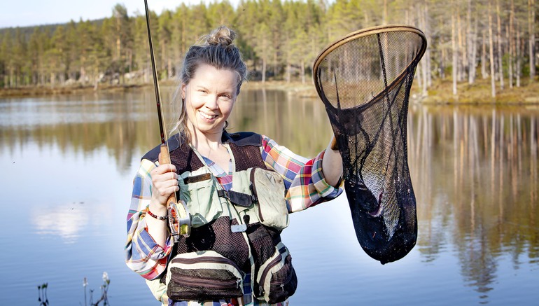 Glad kvinna med fiskeutrustning och en fisk i en håv.
