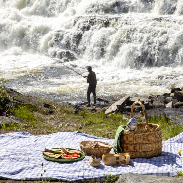 Picknick framför ett vattenfall där det står en fiskare