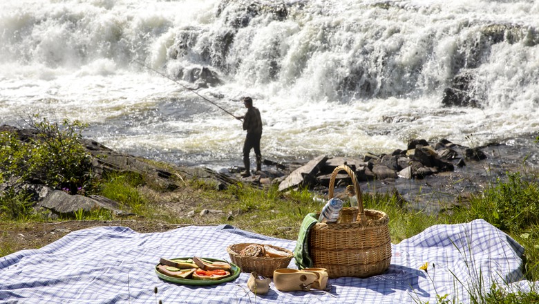 Picknick framför ett vattenfall där det står en fiskare