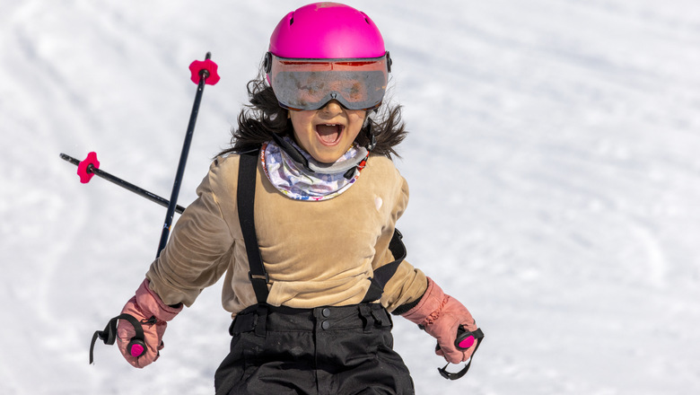 Glad flicka med rosa hjälm åker skidor utför