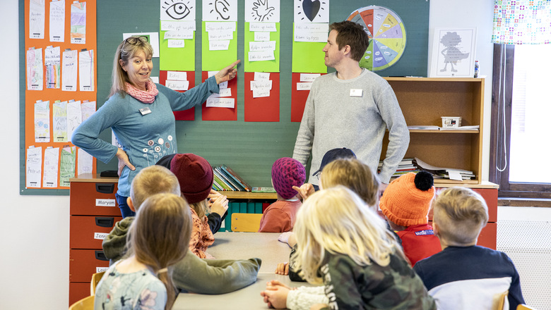 Två lärare pekar på en tavla inför en grupp elever