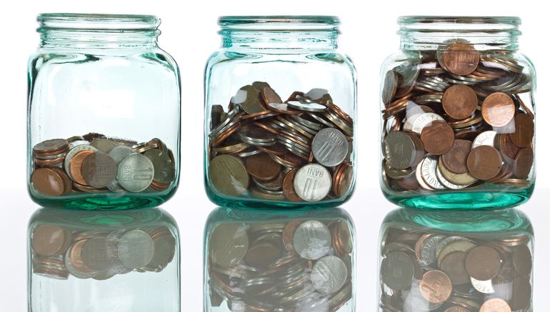 Glass jars with coins on reflective surface, isolated - savings concept