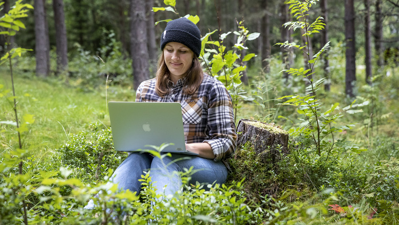 En kvinna mitt i skogen med en dator i knät.