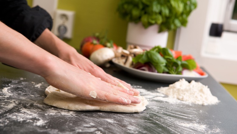Händer som trycker ut pizzadeg i köksmiljö