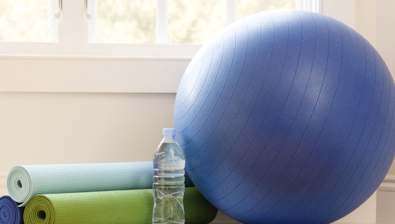 Balance ball, exercise mats and bottled water at gym by window.