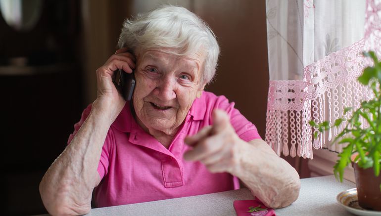 En äldre kvinna sitter vid sitt köksbord och talar i mobiltelefon